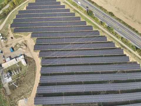 Luftbild einer Freiflächen-Photovoltaikanlage mit Umspannwerk, daneben eine Autobahn