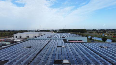 Große Photovoltaikanlage auf dem Flachdach einer Logistikhalle, im Hintergrund Windenergieanlagen