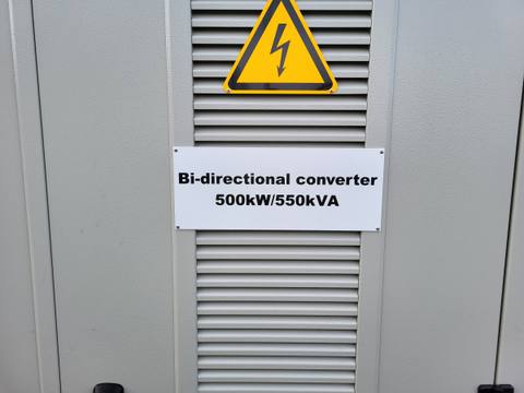 Lüftungsgitter eines Speicherumrichters mit Schild „Bi-directional converter 500 kW / 550 kVA“ und Warnzeichen für elektrische Spannung