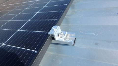 Nahaufnahme einer Modulklemme am Rand eines PV-Moduls auf einem Trapezblechdach