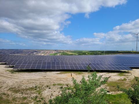 Freiflächen-Photovoltaikanlage auf einer ehemaligen Bergbaufläche, am Horizont eine Windenergieanlage