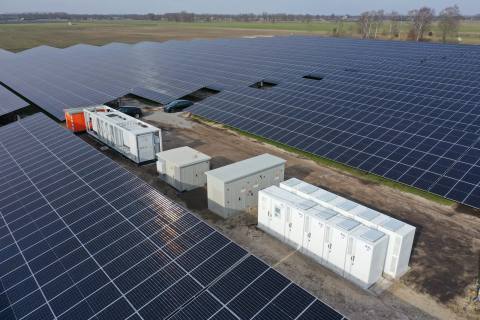 Drohnenaufnahme einer PV-Freiflächenanlage mit Batteriespeicher-Containern, Transformatorstationen und Wechselrichtern zwischen den Modulreihen