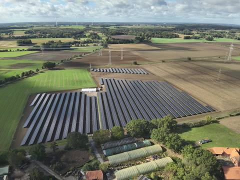 Wide aerial view over a flat agricultural landscape with a ground-mounted photovoltaic installation and high-voltage lines