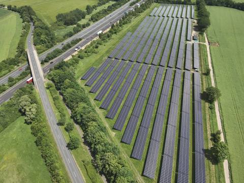 Aerial view of a ground-mounted photovoltaic system between a road and a railway line