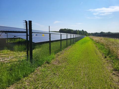 Fence with posts at the edge of a ground-mounted system, next to it a mown maintenance path and the first module row