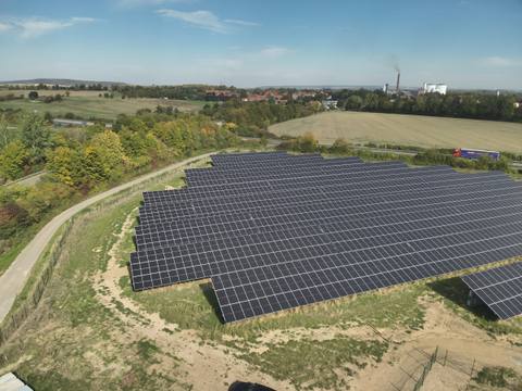 Aerial view of a ground-mounted photovoltaic installation on a gentle slope between woodland and fields